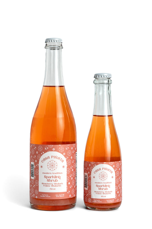 Two bottles of Casa Piñata Strawberry Shrub, one 375ml and one 750ml clear champagne bottle, against a white background.