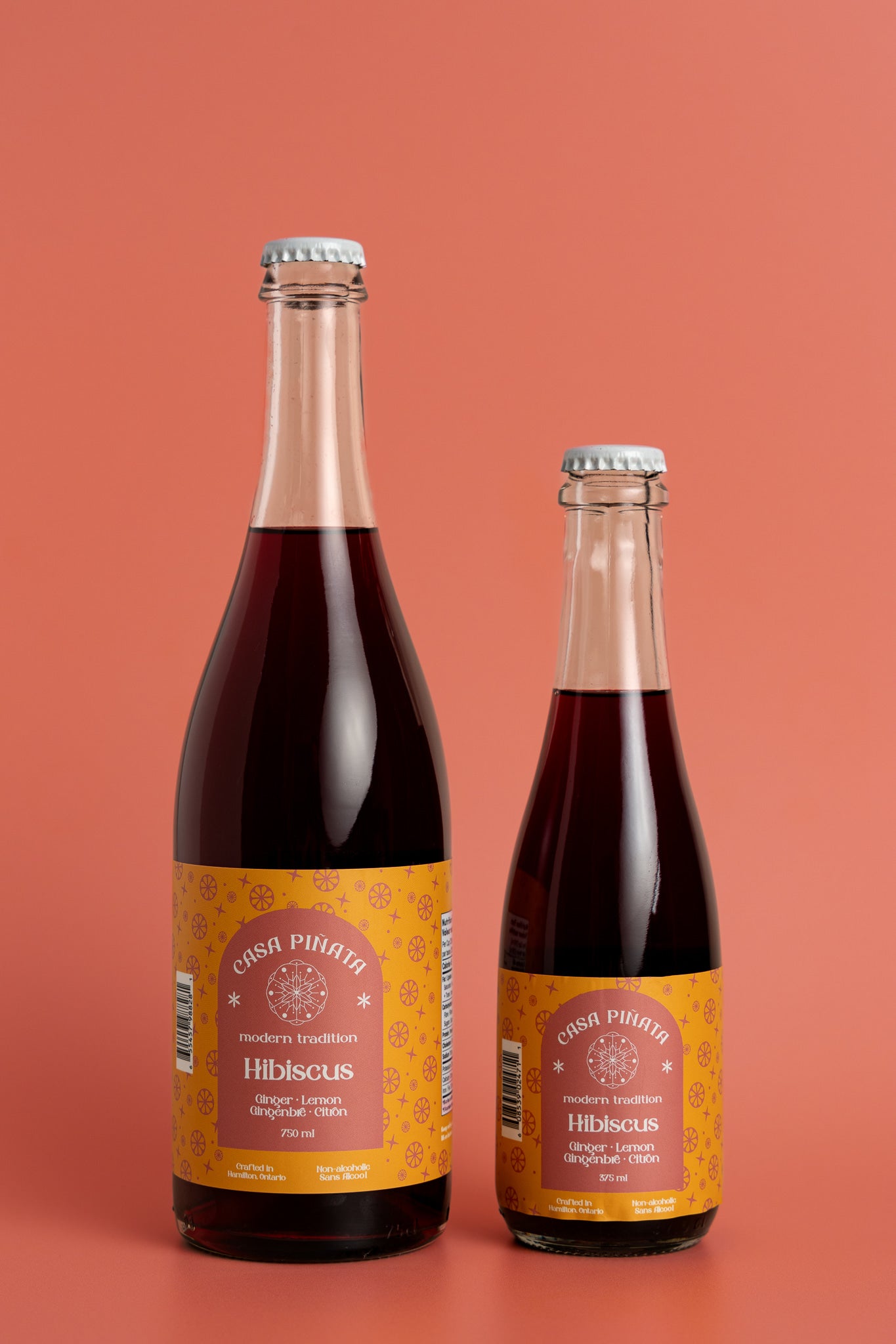 Two bottles of Casa Piñata hibiscus spritzer, one 375ml and one 750ml clear champagne bottle, against a red background.