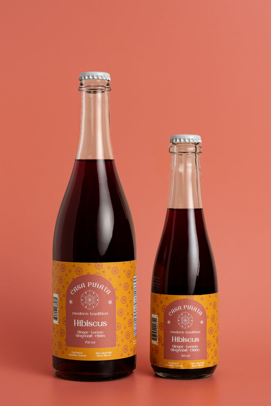 Two bottles of Casa Piñata hibiscus spritzer, one 375ml and one 750ml clear champagne bottle, against a red background.
