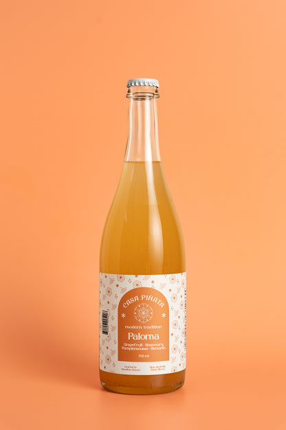 750 ml clear champagne bottle of Casa Piñata Paloma Mocktail against a pink background.