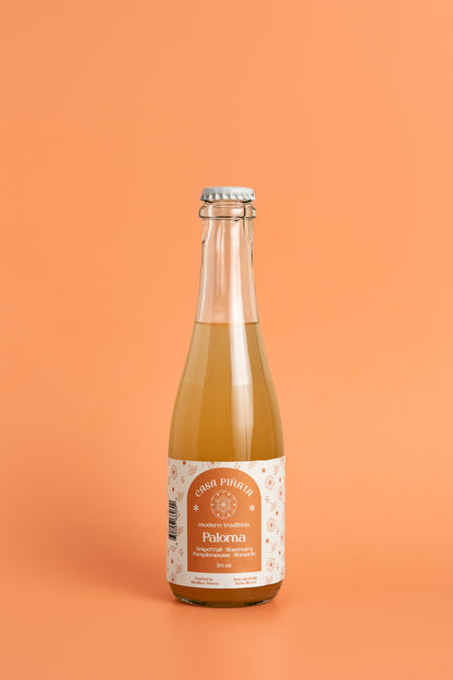 375 ml clear champagne bottle of Casa Piñata Paloma Mocktail against a pink background.